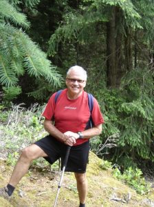 Raymond Thompson on hillside in red T-shirt and black shorts with backpack and walking stick