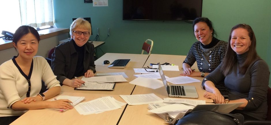 Four scholars, including Elsie, smile for the camera in a small meeting room with a laptop and papers spread on the table.